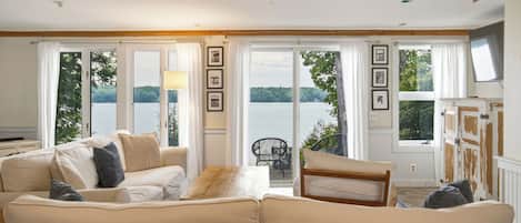 A living room with a sofa, a coffee table, and a view of a lake through large windows.