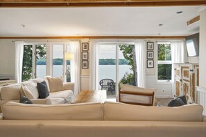 A living room with a sofa, a coffee table, and a view of a lake through large windows. - Highland Lake Cottage/Waterfront/Dock/Kayaks (Windham)