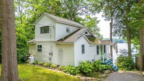 A two-story house with a porch, surrounded by trees and a body of water. - Highland Lake Cottage/Waterfront/Dock/Kayaks (Windham)