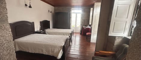 Une chambre avec deux lits, un plafond en bois, une petite table avec une chaise, et une vue sur l’extérieur par une porte ouverte.