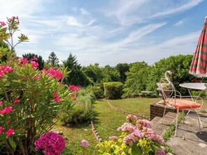 A garden with a metal table and chairs, a swan-shaped birdbath, and various flowering plants. - Maison Rose by Interhome (Deauville-Trouville)
