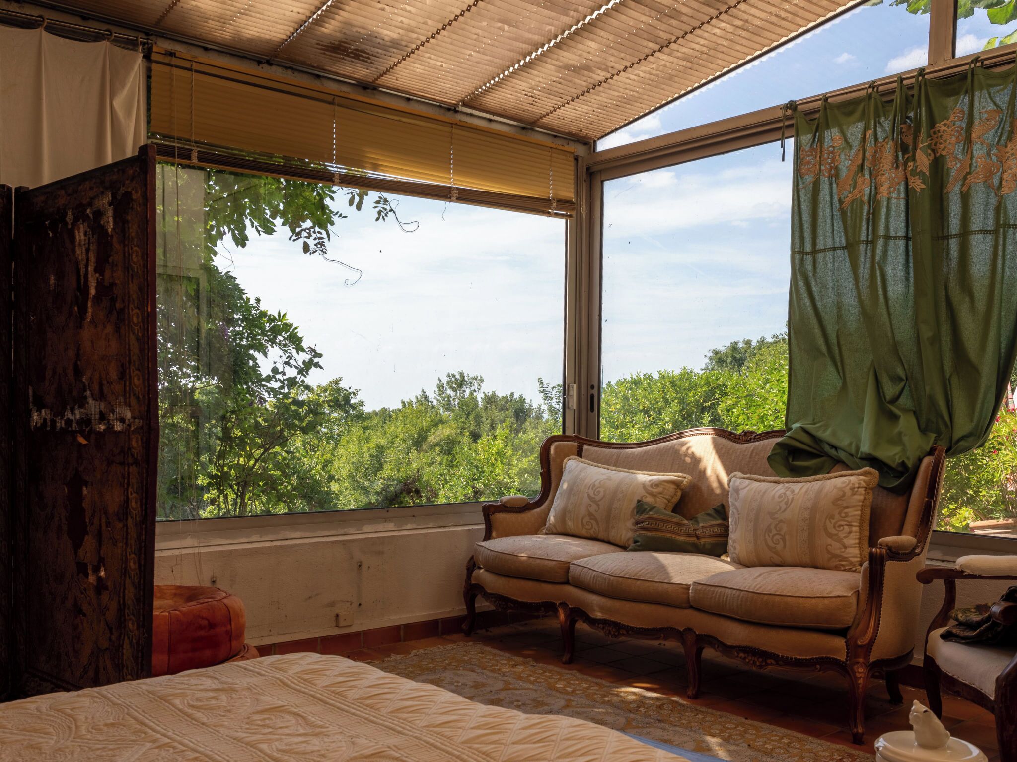 A room with a large window, a wooden bench, a bed, and a chair.
