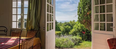 An open room with a table and chairs, a view of greenery and a red rooster statue outside.
