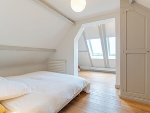 Ett sovrum med ett sluttande tak, en säng, ett element och en garderob.