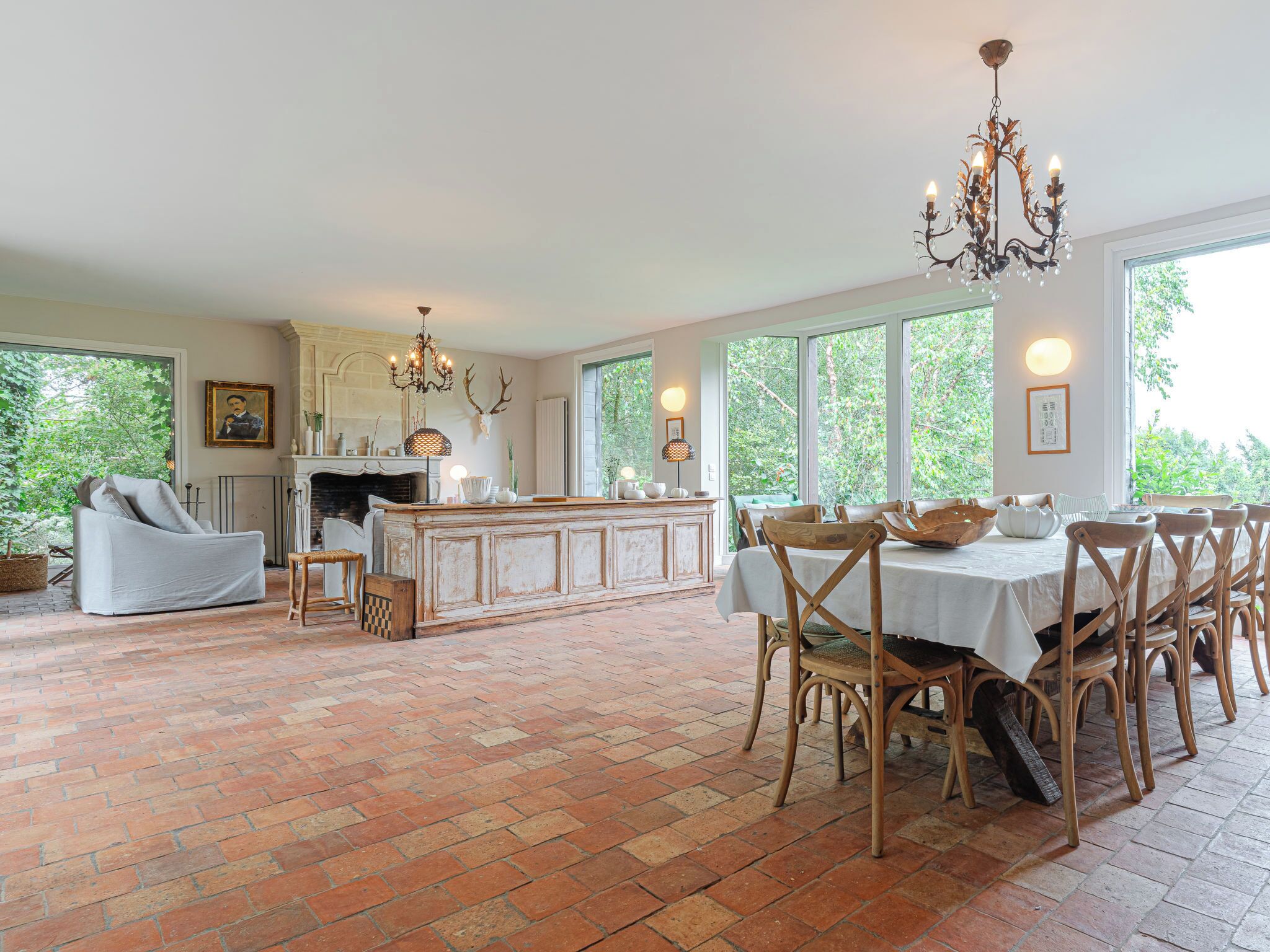 A spacious room with a brick floor, a dining table with chairs, a fireplace, and large windows.