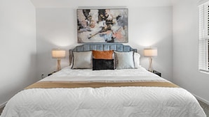 A bedroom with a large bed, a tufted headboard, two bedside lamps, and a painting above the bed. -     Spacious Katy TX  one story Home / 4 Bedrooms + Hot Tub (Katy)
