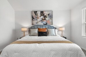 A bedroom with a large bed, a tufted headboard, two bedside lamps, and a painting above the bed.