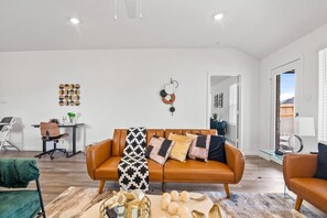 A modern living room with a leather sofa, a glass coffee table, and a desk with a chair.