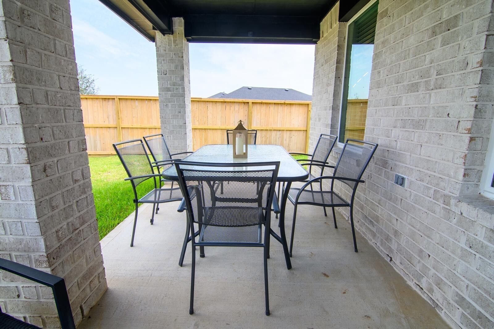 An outdoor patio with a table and chairs, surrounded by brick walls, with a wooden fence and grass in the background.