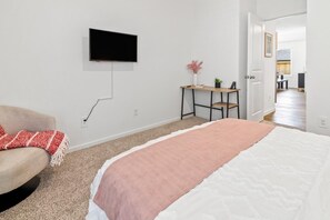 A bedroom with a bed, a TV mounted on the wall, a desk with a chair, and a door leading to another room. -     Spacious Katy TX  one story Home / 4 Bedrooms + Hot Tub (Katy)