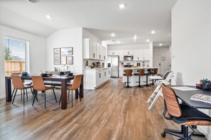 A modern kitchen with white cabinets, a dining area with wooden chairs, and a bar area with stools.