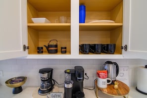 A kitchen with two open cabinets, a coffee station, and a sign reading 'HOME SWEET HOME'.
