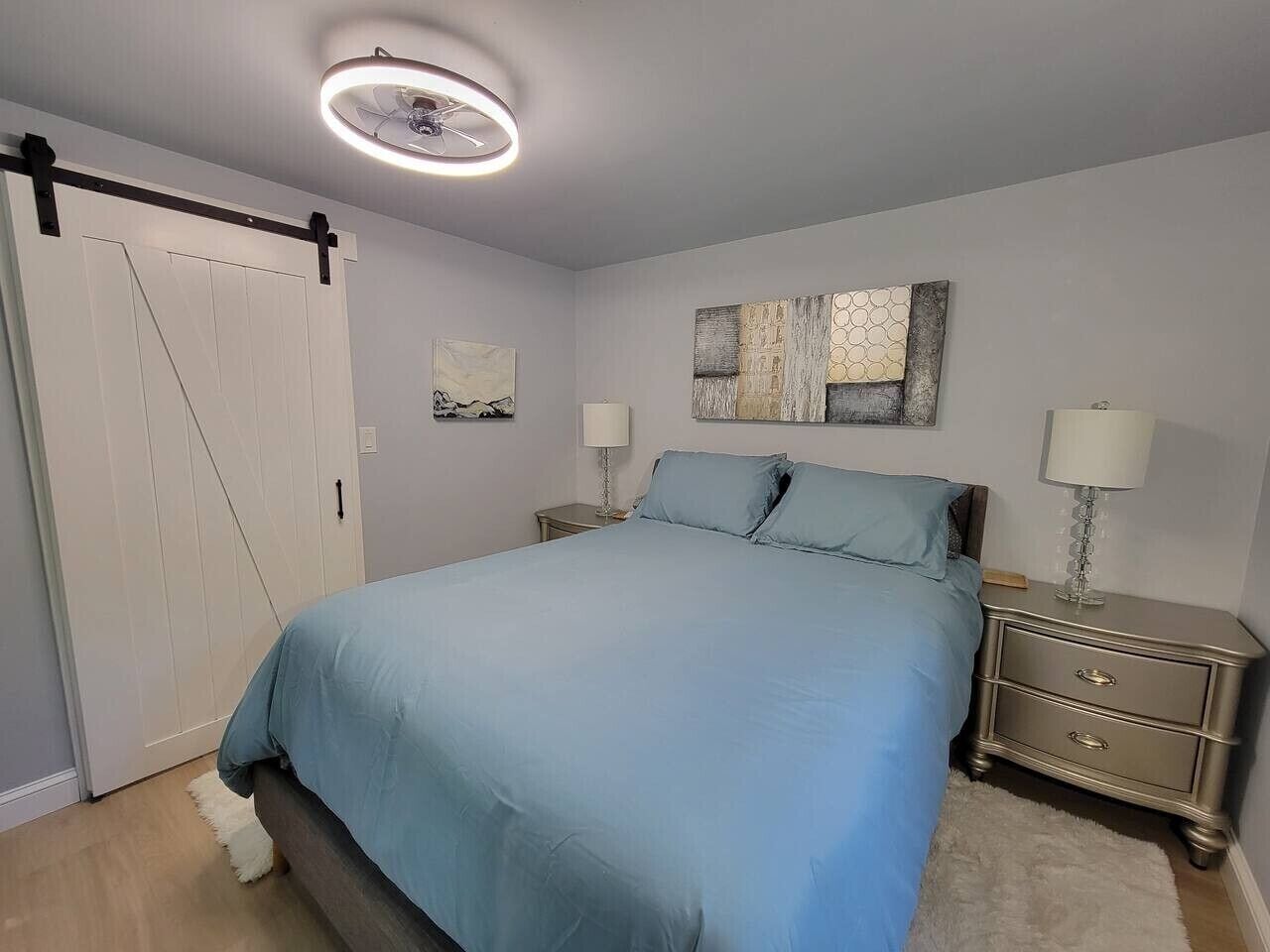 Un dormitorio con cama, mesitas de noche, una obra de arte en la pared y una lámpara del techo.