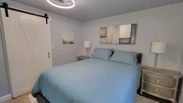 Un dormitorio con cama, mesitas de noche, una obra de arte en la pared y una lámpara del techo.