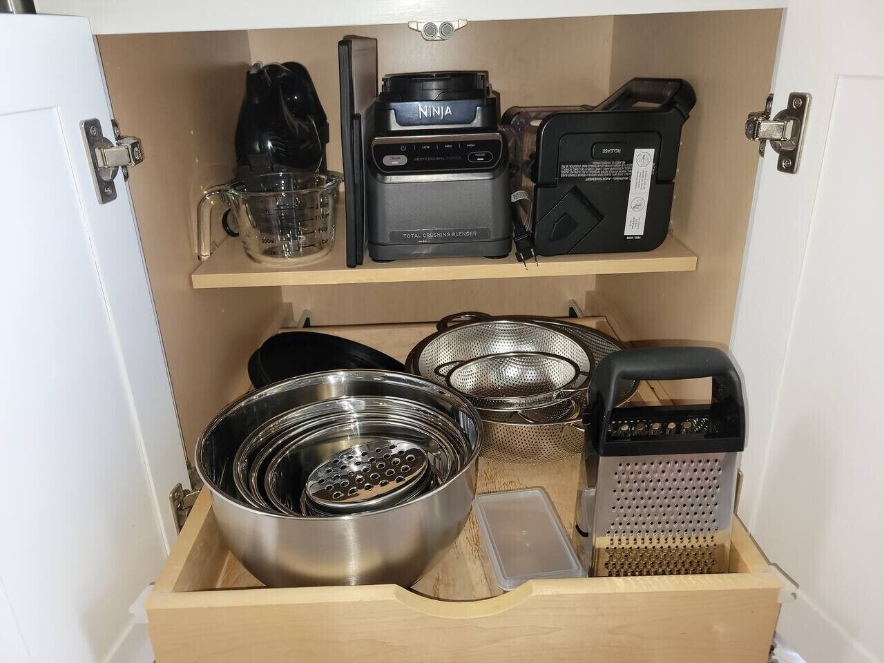 A kitchen drawer with a Ninja total crushing blender, a kettle, a grater, and various kitchen utensils.