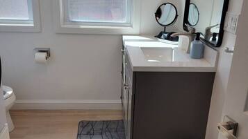 Un baño con un lavamanos blanco, dos espejos, un perchero y un cubo de basura.