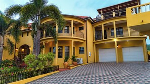 Un edificio amarillo de varios pisos con balcones, un garaje y un camino de entrada con baldosas estampadas.