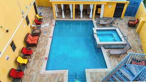 Una piscina con varias zonas de estar y un jacuzzi pequeño.