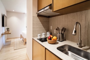 A modern kitchen with a stainless steel sink, wooden cabinets, a built-in stove, and a fruit bowl on the counter. - Laiva Artwalk by Tasman (San José del Cabo)