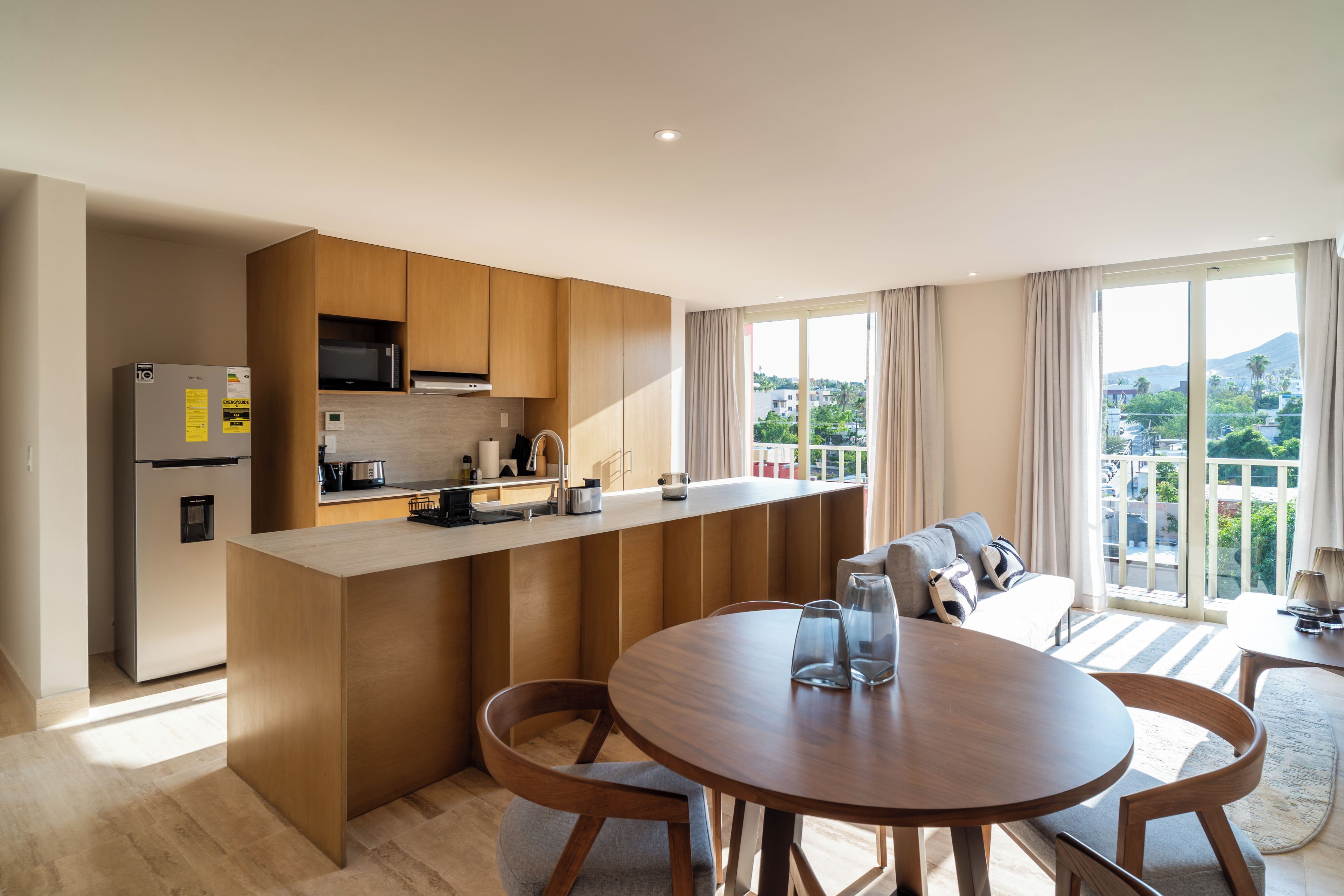 Een moderne keuken met een centraal eiland, een eettafel met stoelen en een stadsgezicht door grote ramen.