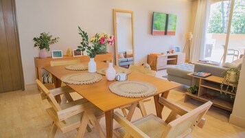 Un comedor con una mesa de madera, sillas tejidas y un espejo en la pared.