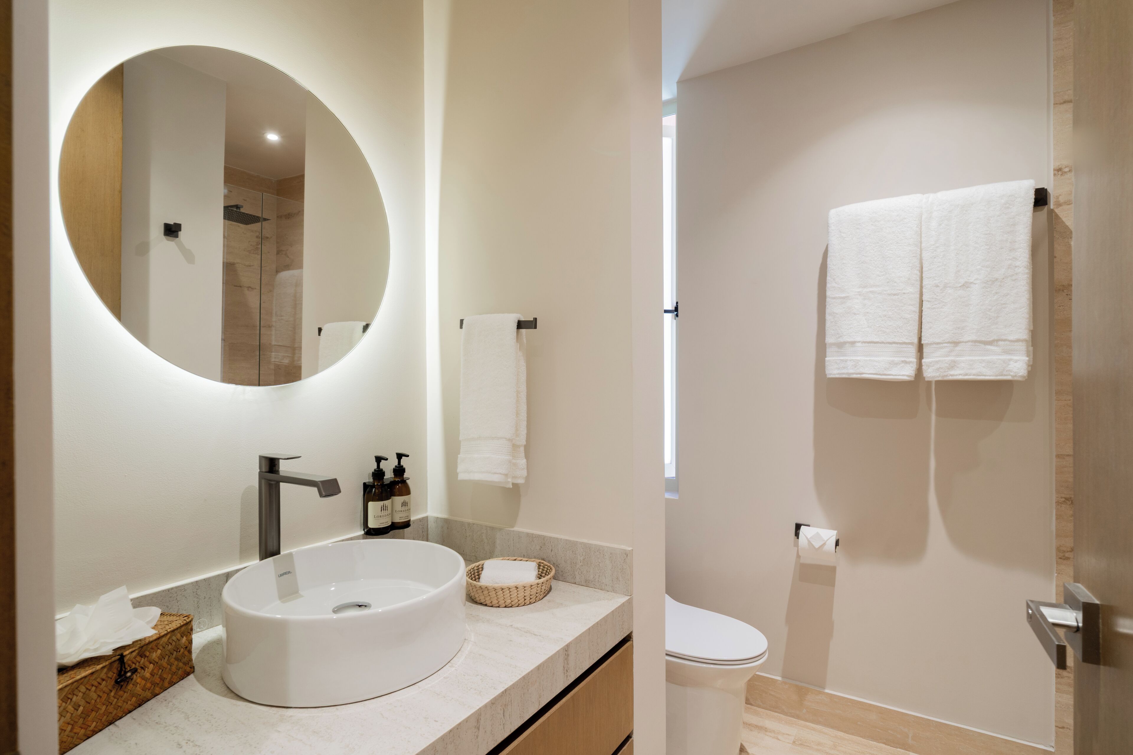 Een moderne badkamer met een ronde spiegel, een wastafel, toilet en douche.
