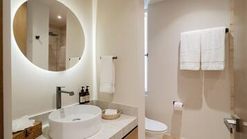 Een moderne badkamer met een ronde spiegel, een wastafel, toilet en douche.
