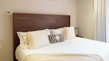 Une chambre d’hôtel avec une tête de lit en bois, un lit avec une literie blanche, un plaid et un climatiseur fixé au mur.