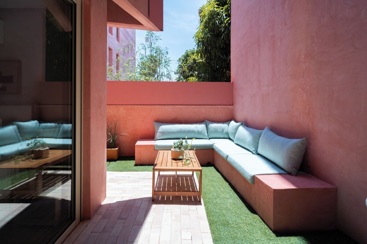 A modern outdoor seating area with a sectional sofa, a wooden coffee table, and a glass partition.