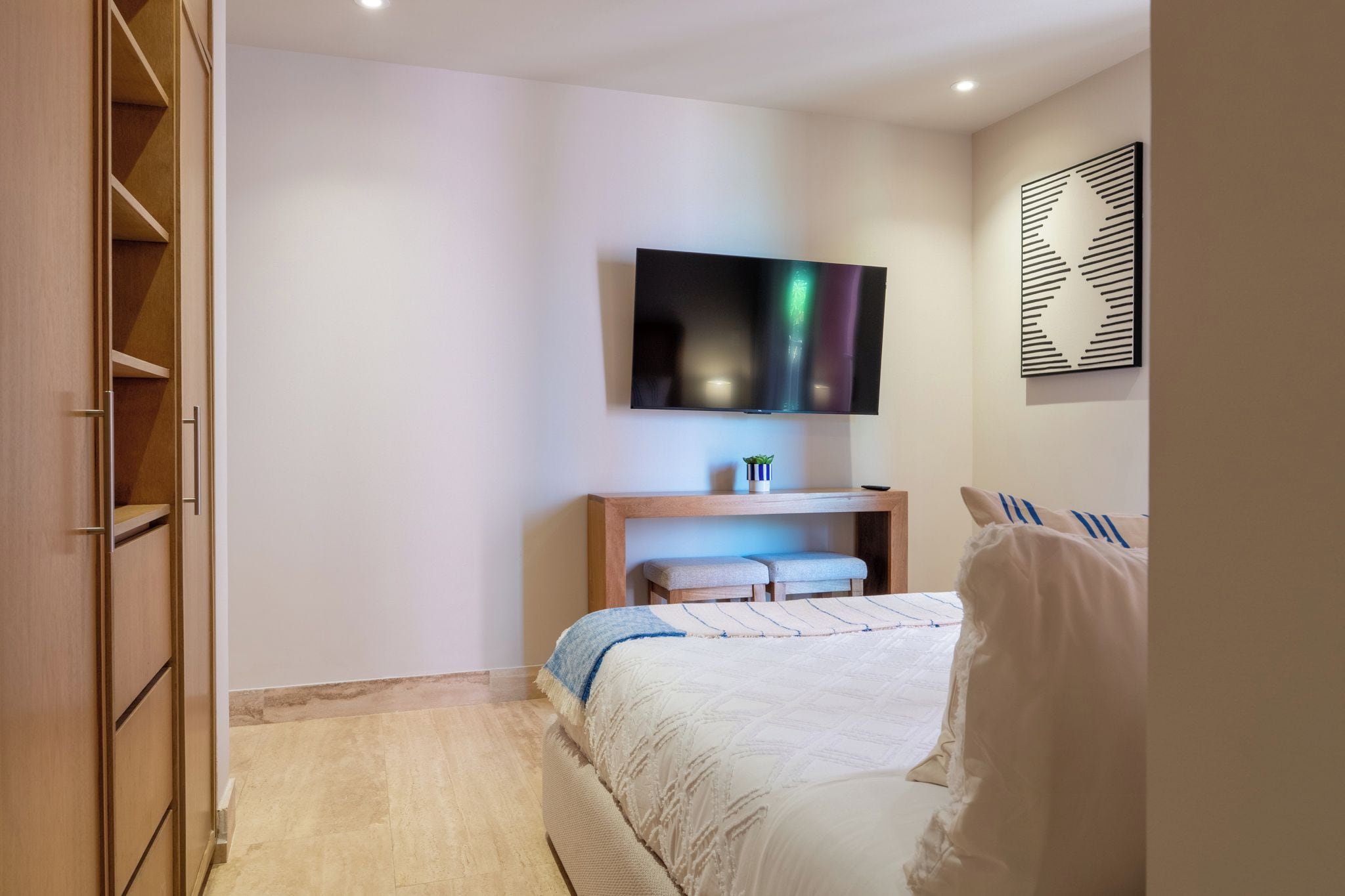 A bedroom with a bed, a TV mounted on the wall, a wooden cabinet, and a small plant.