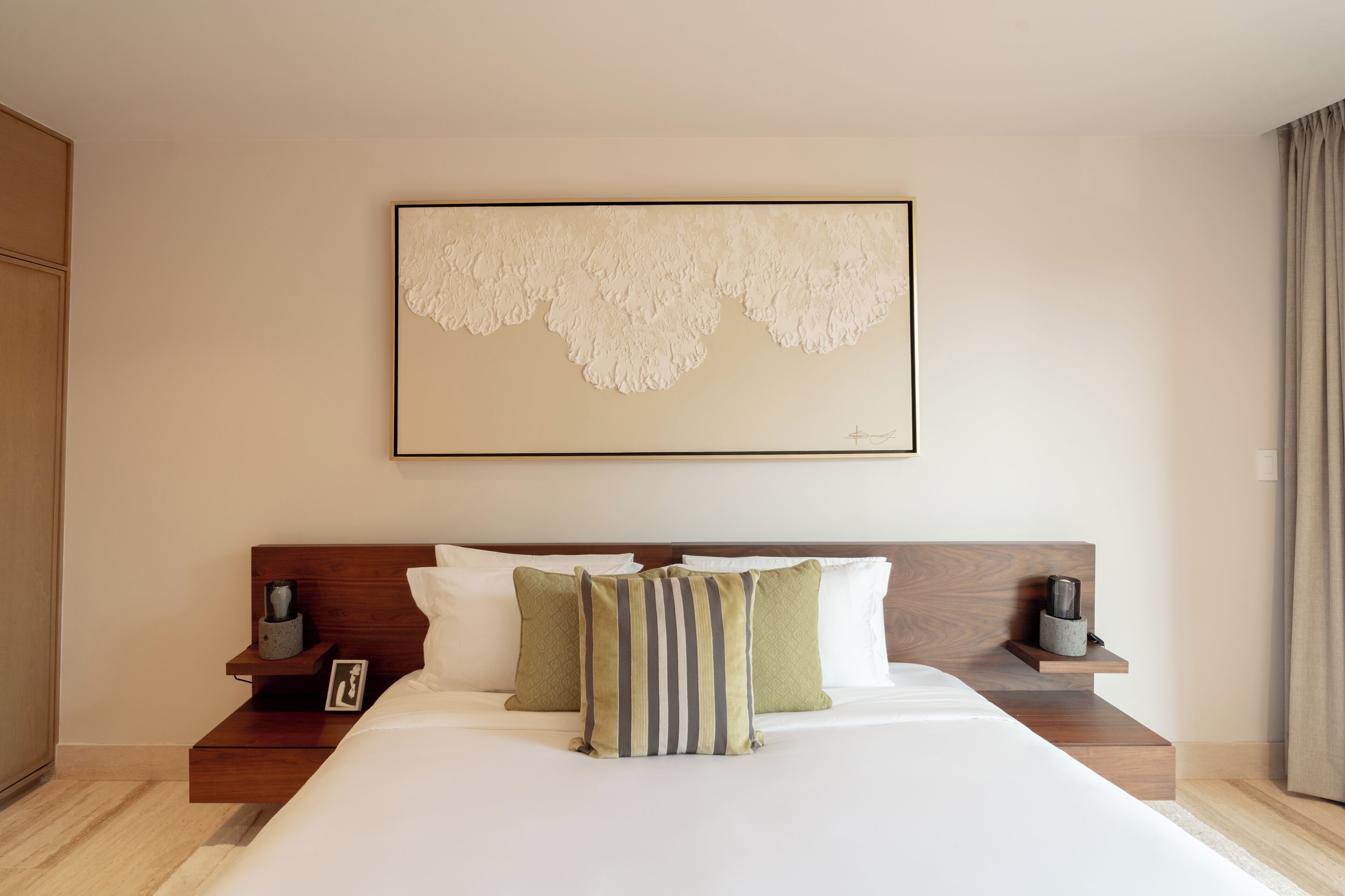 Una habitación de hotel con una cama grande, dos mesitas de noche, una obra de arte enmarcada sobre la cama y un cabecero de madera.