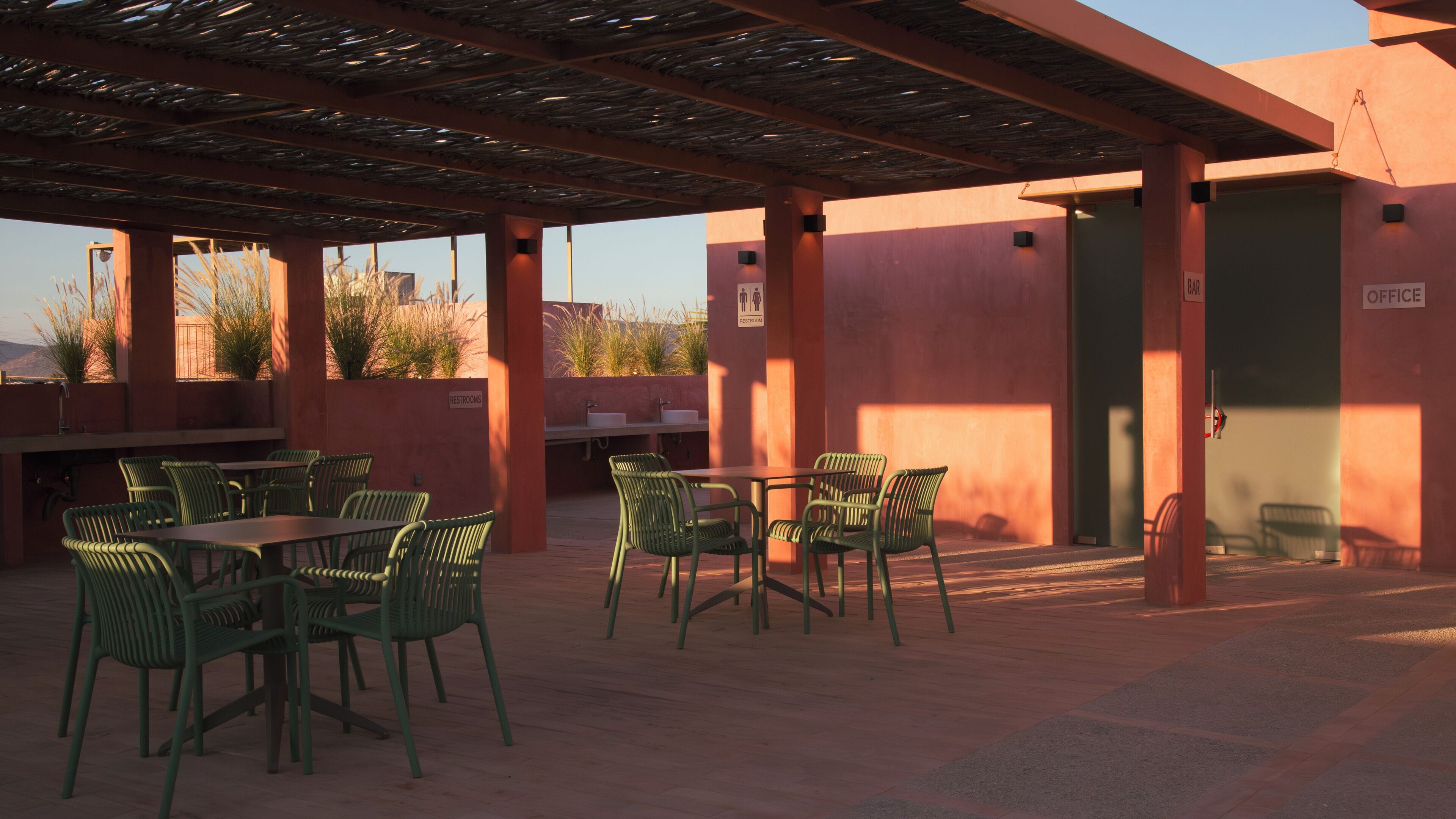 An outdoor patio area with green chairs and tables, a bar, and a restroom sign.
