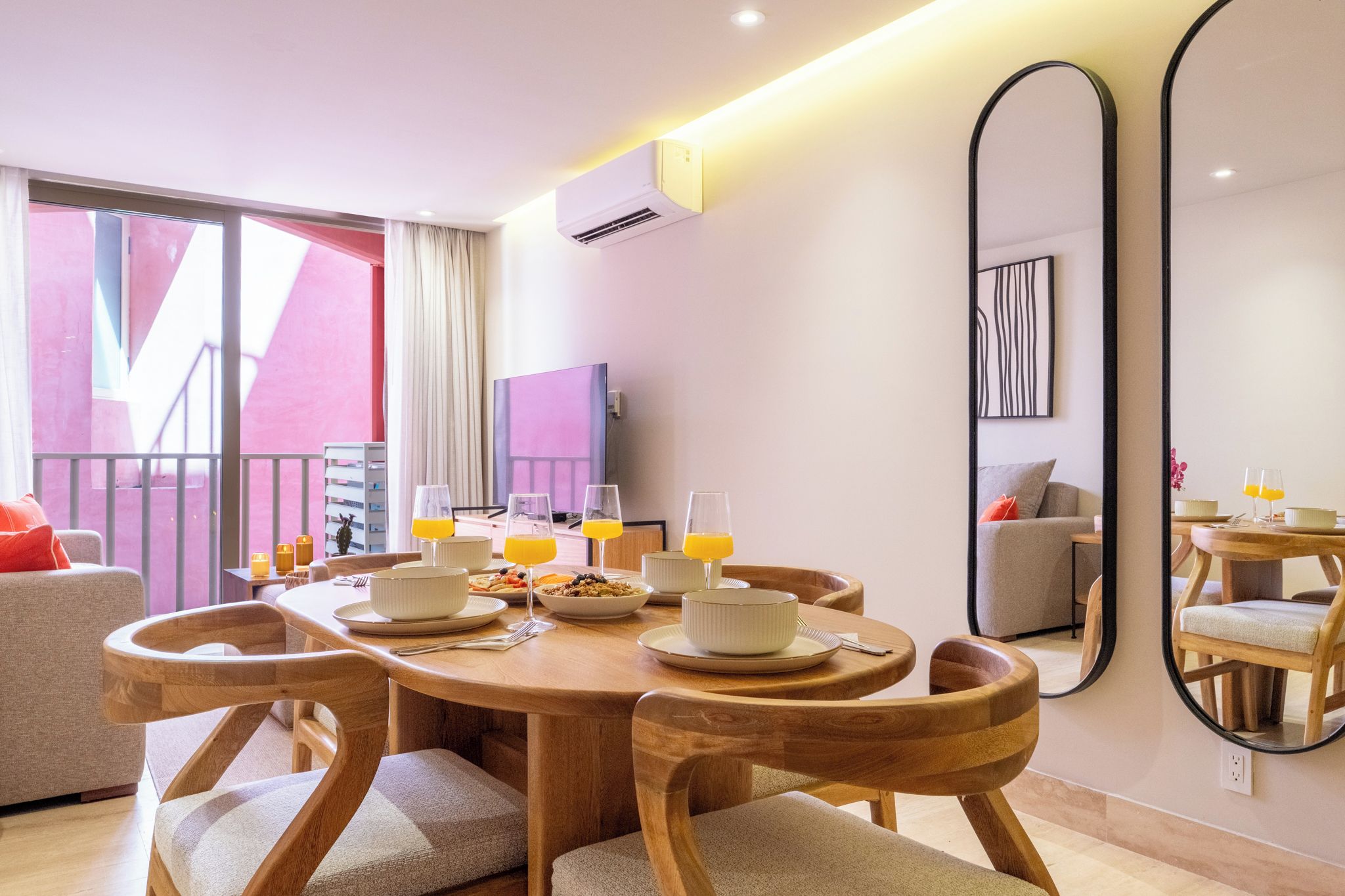A modern dining area with a round wooden table, white plates, and glasses of orange juice.