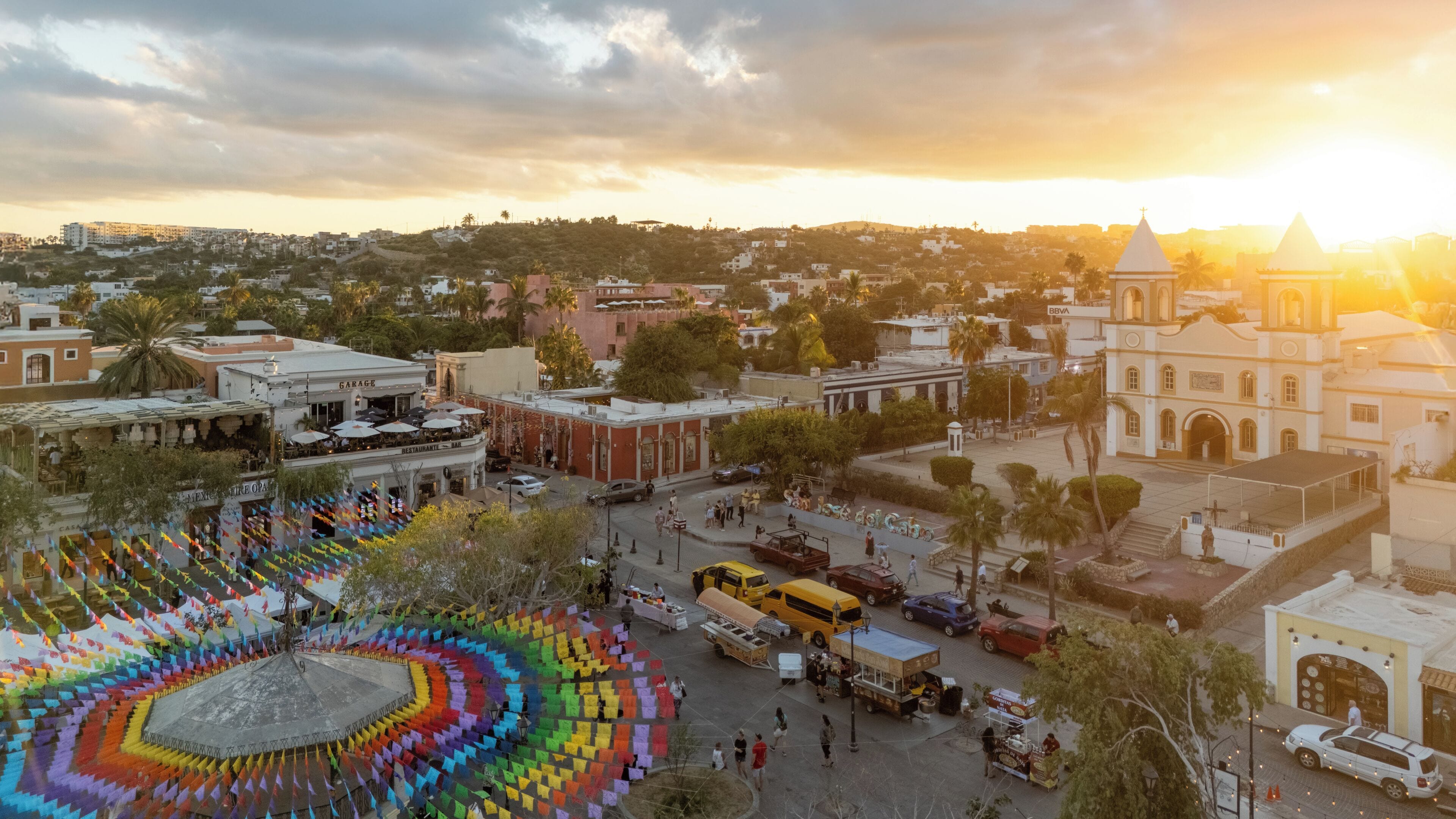 A plaza with colorful flags, a church, and a mix of commercial and residential buildings.