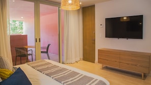 A bedroom with a bed, a TV, a wooden dresser, and a sliding glass door leading to an outdoor area. - Laiva Artwalk by Tasman (San José del Cabo)