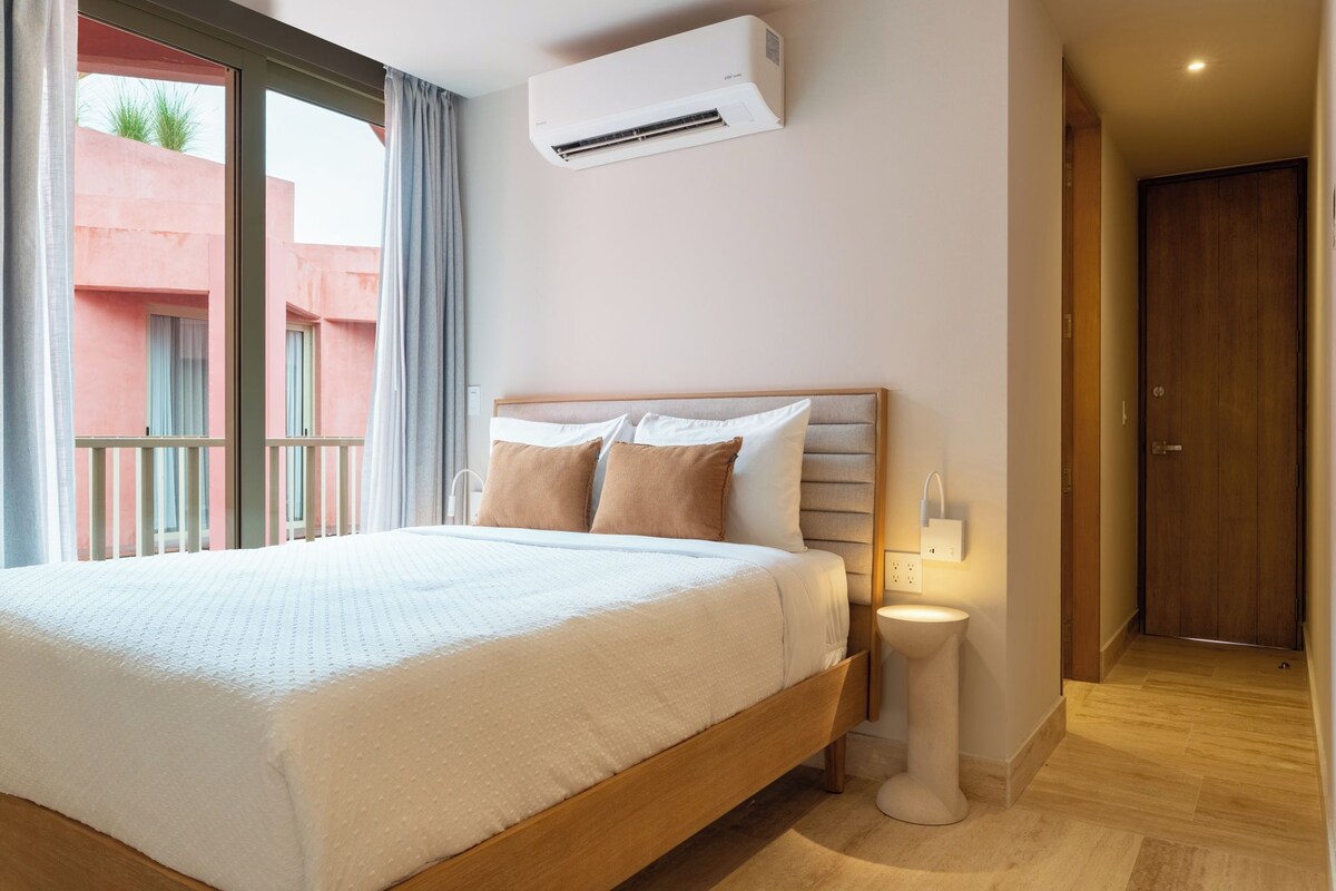 Una habitación de hotel con cama, mesita de noche y aire acondicionado.