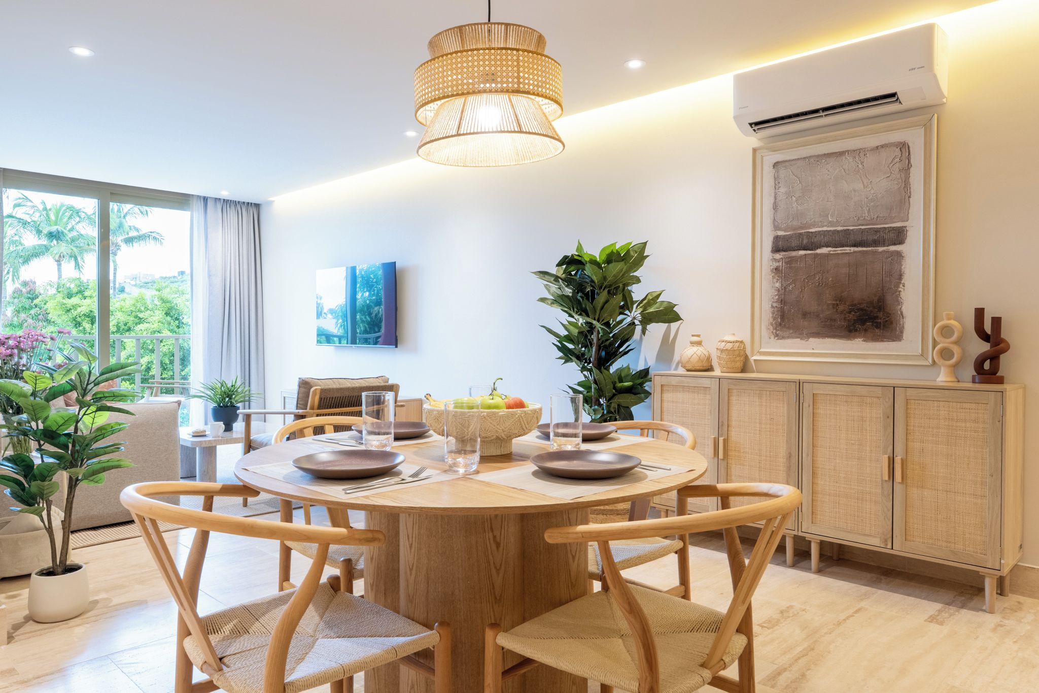 A modern dining area with a round wooden table, chairs, and a hanging light fixture.