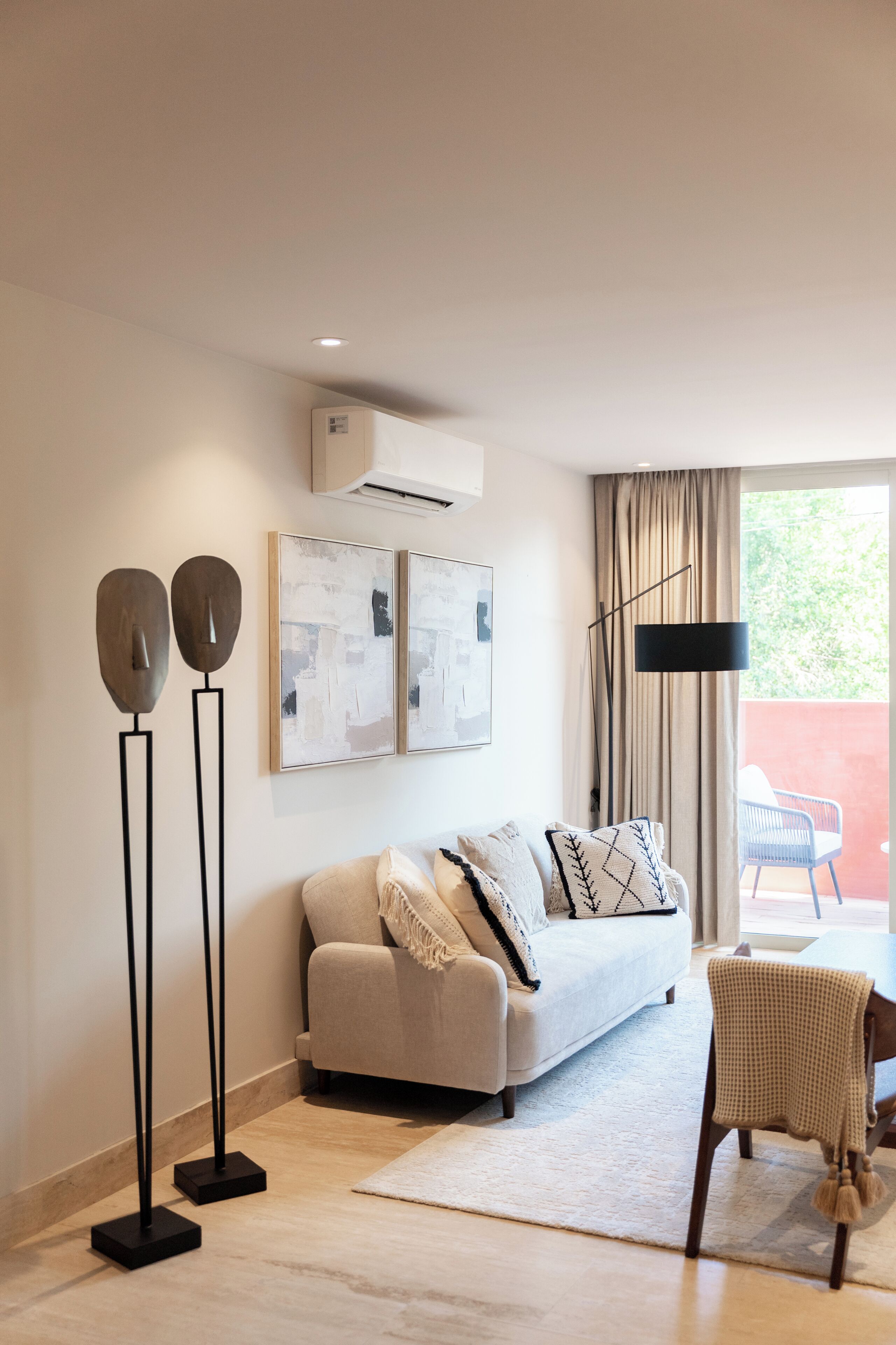 A modern living room with a sofa, a coffee table, and a chair. There is a large window with curtains, a floor lamp, and wall-mounted artwork.