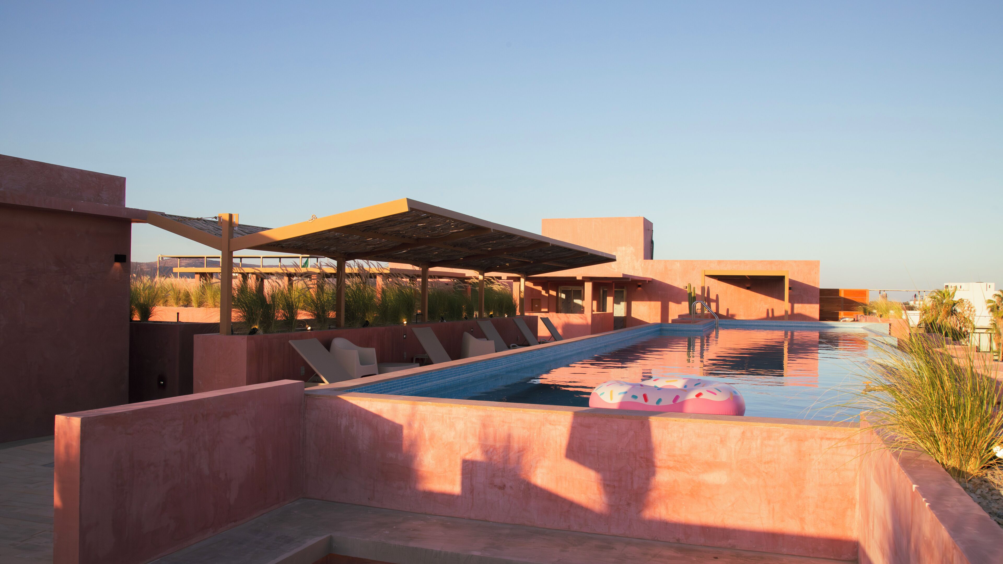 A swimming pool with lounge chairs and a covered area, surrounded by buildings.