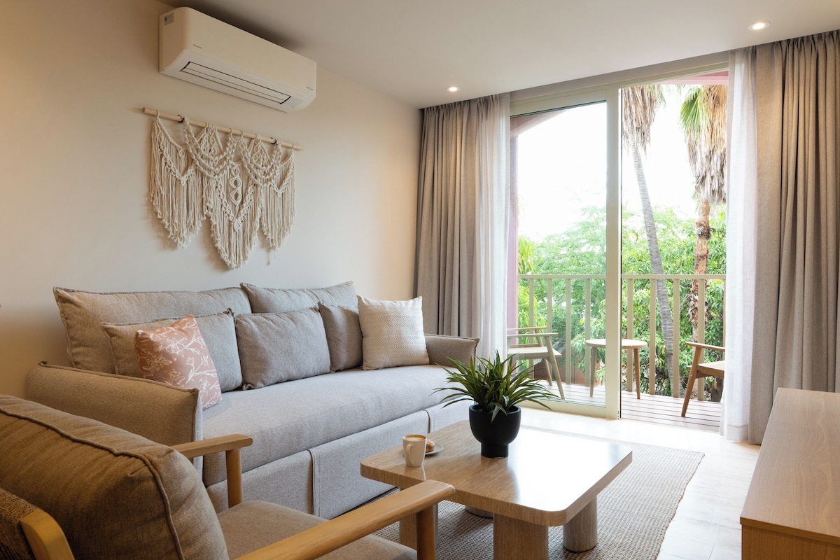 A modern living room with a sofa, coffee table, and a balcony with a view of greenery.
