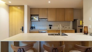 A modern kitchen with wooden cabinets, a built-in microwave, a stainless steel sink, and a bar area with bar stools. - Laiva Artwalk by Tasman (San José del Cabo)
