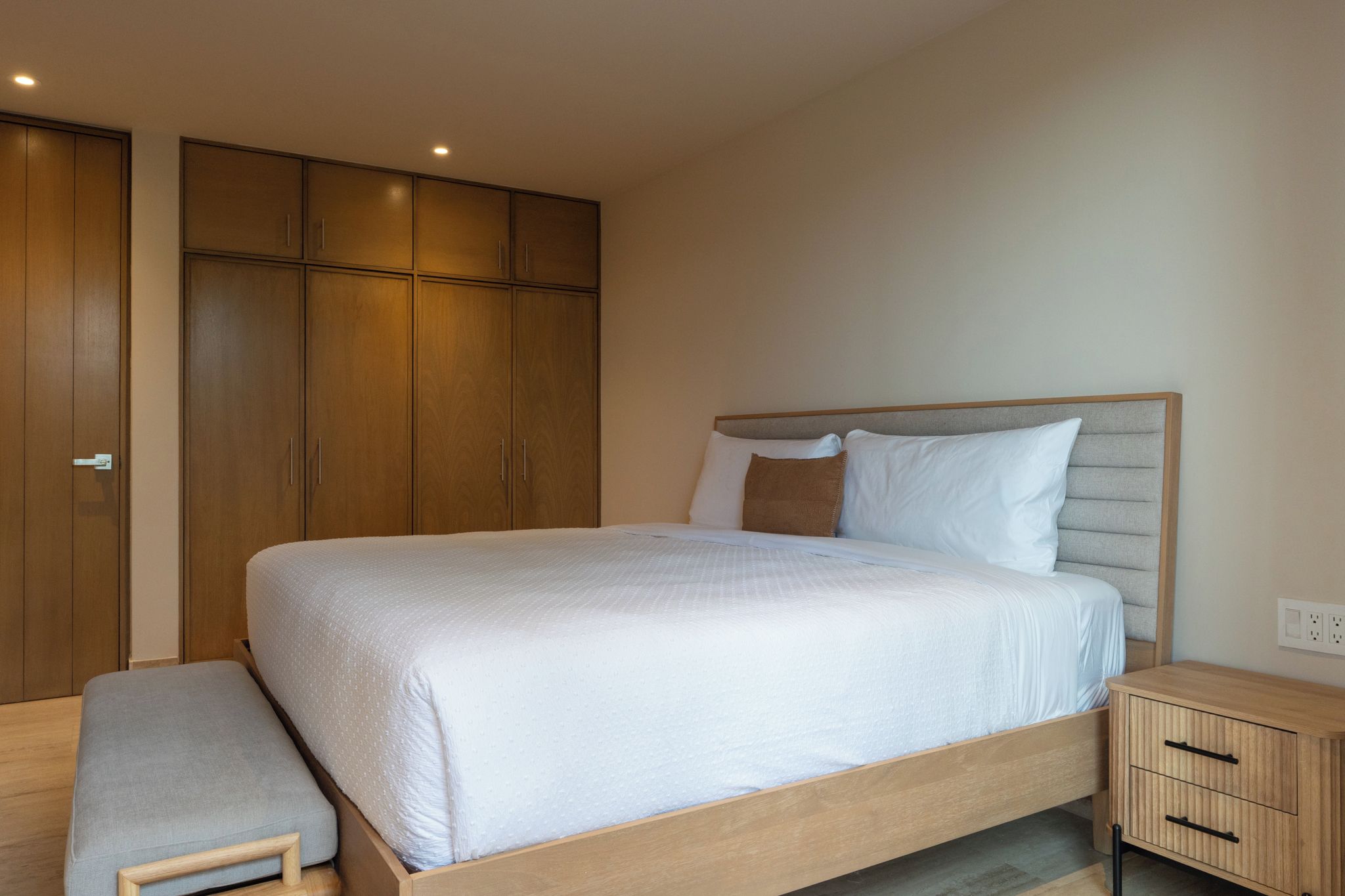 A bedroom with a bed, a bench, a nightstand, and wooden wardrobes.