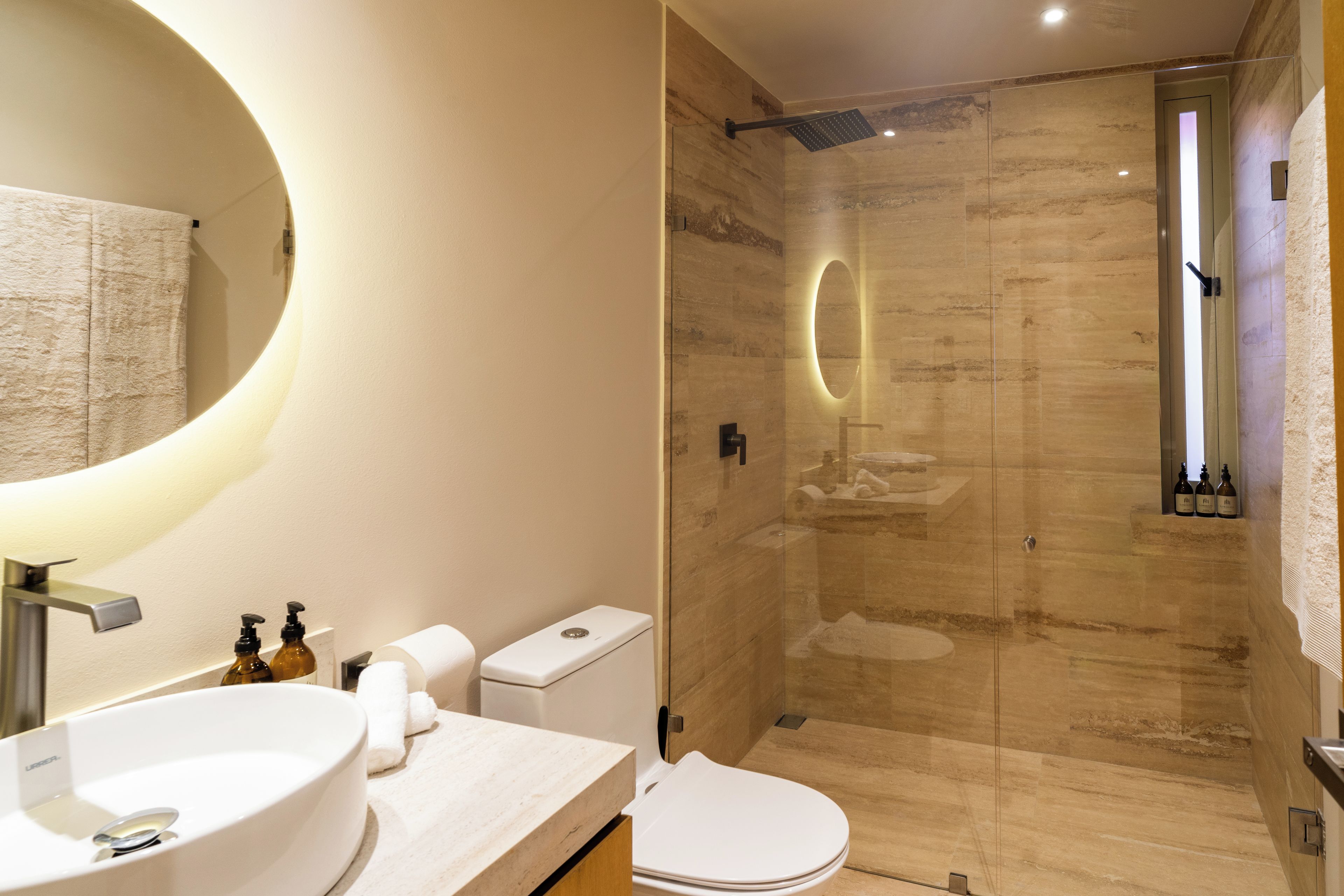 A modern bathroom with a round mirror, a sink, a toilet, and a shower area.