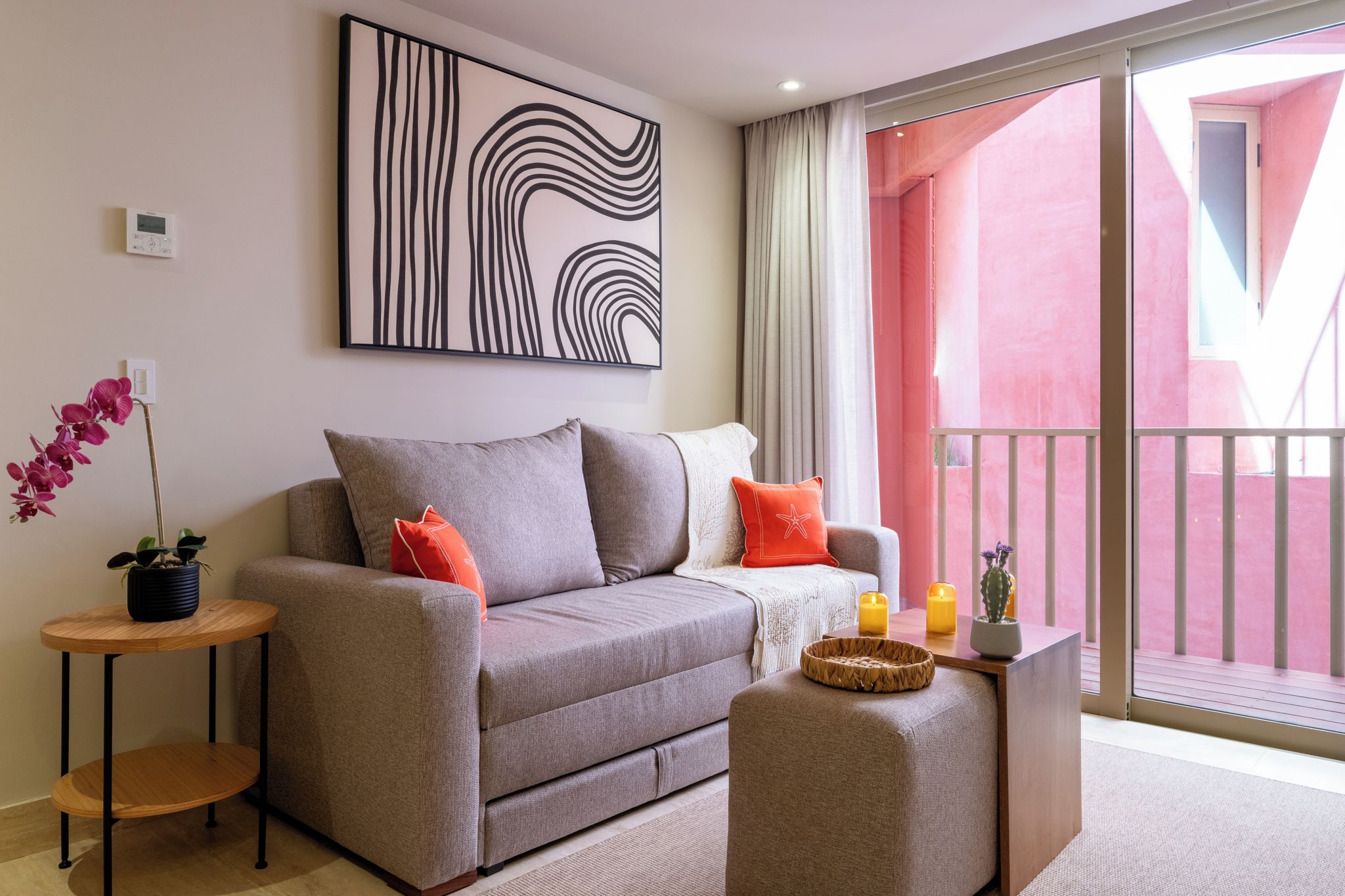 Un salon moderne avec un canapé gris, deux coussins rouges, une table d’appoint sur laquelle est posée une plante en pot, et un grand tableau abstrait accroché au mur.