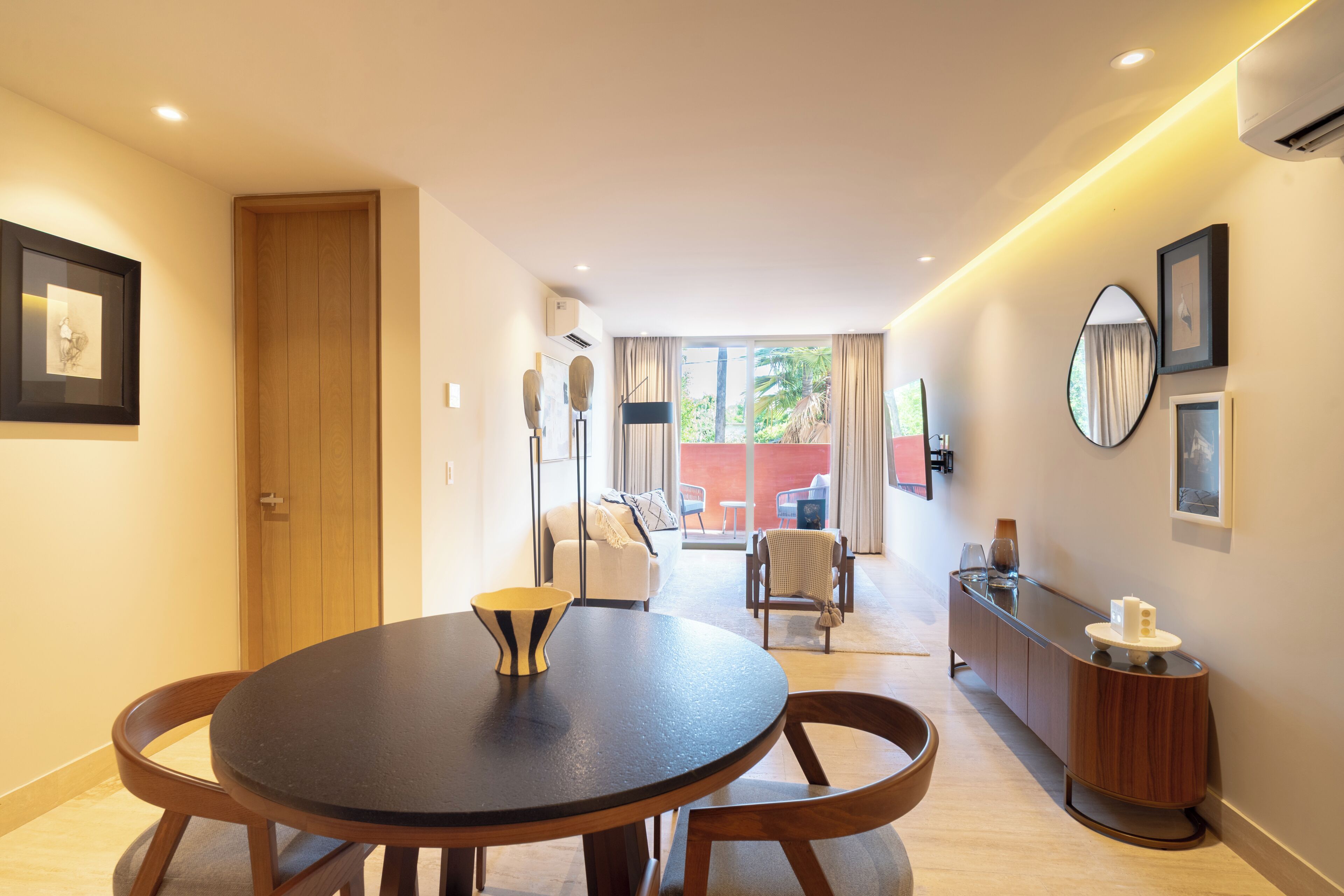 A modern hotel room with a round dining table, a sofa, a chair, and a small cabinet.