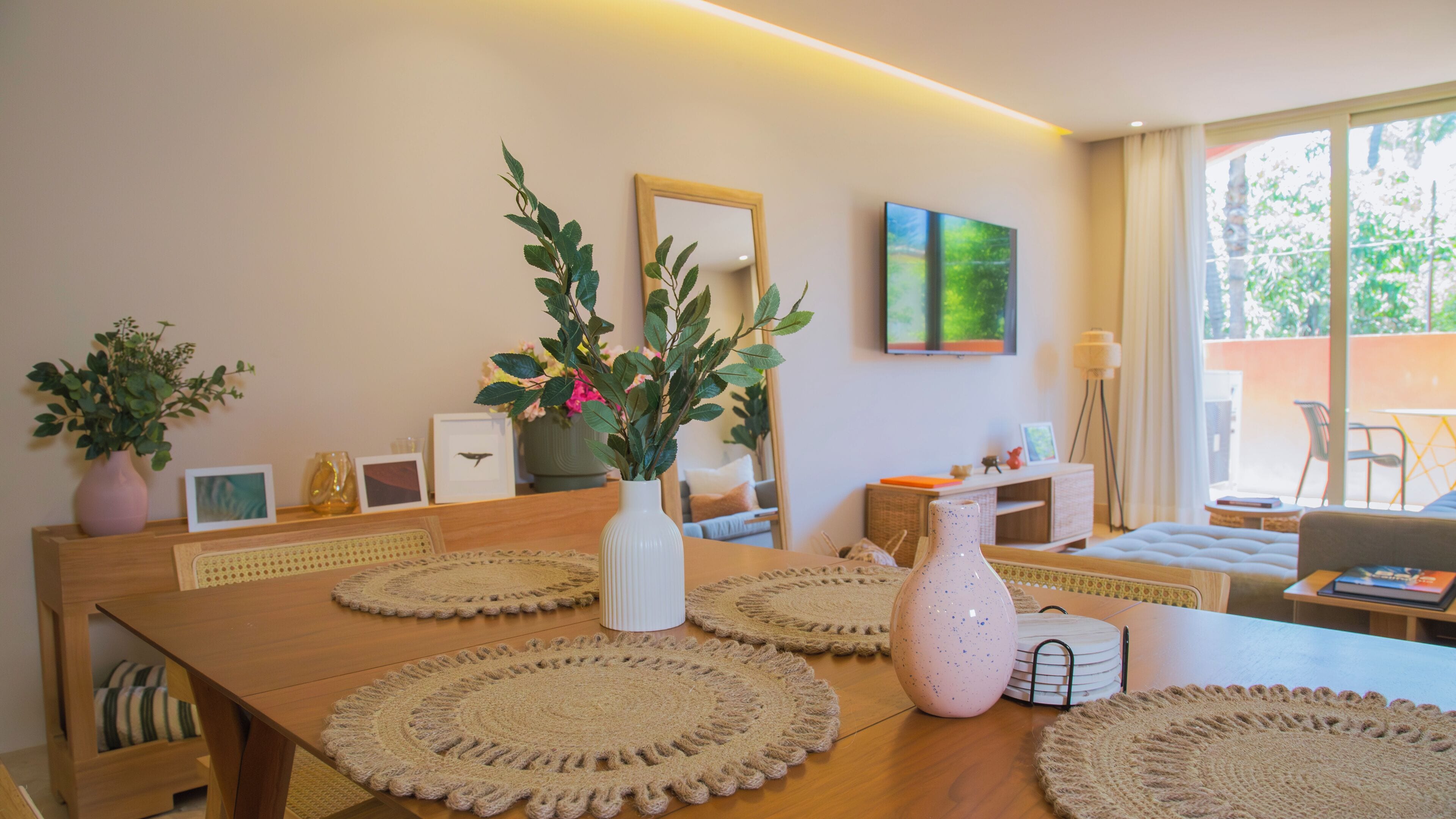 Un comedor con una mesa de madera, individuales de crochet y un jarrón con plantas.