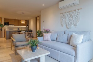 A modern living room with a grey sofa, a wooden coffee table with a plant, and a kitchen in the background.