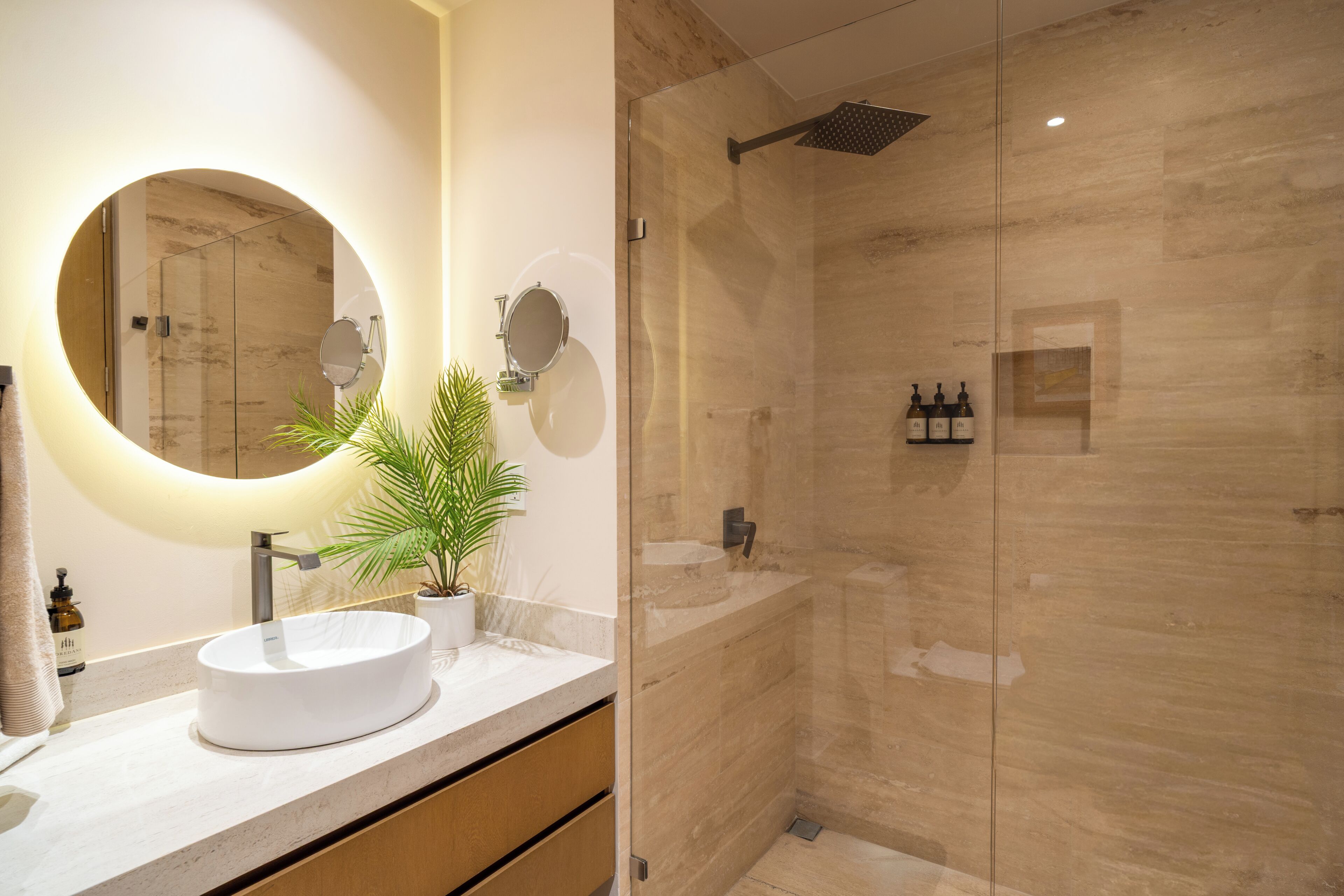 A modern bathroom with a round mirror, a vessel sink, and a glass-enclosed shower area.