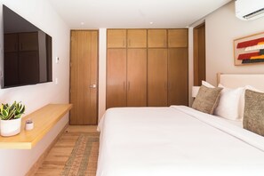 A bedroom with a bed, a TV mounted on the wall, a wardrobe, and a small plant on a shelf.