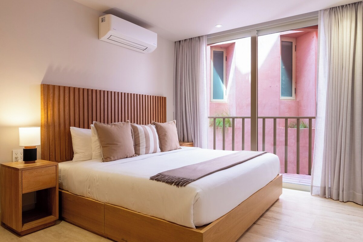 A hotel room with a bed, bedside table, and a window with curtains.